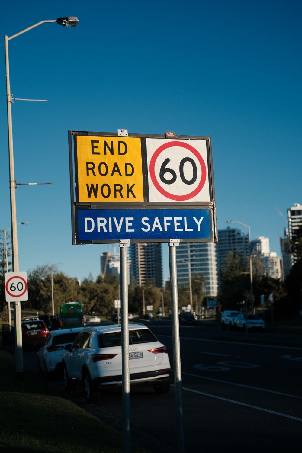 End Road Work sign with a 60 km/h speed limit and Drive Safely plate on a city road